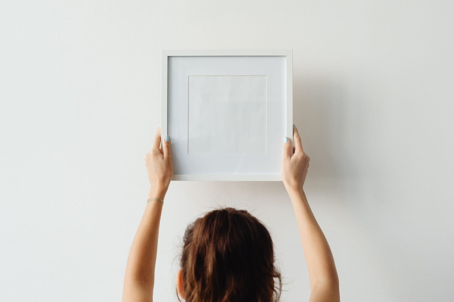 Hands pressing a framed print flat against a pale painted wall